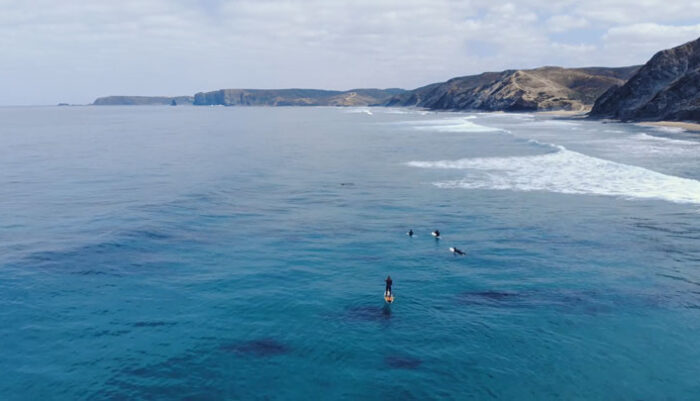Aerial Footage Of Surfer Paddling Across The Sea With Scenic View Of The Mountains